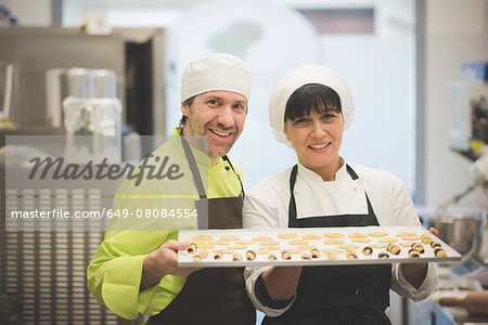 Bakers carrying tray of pastries in kitchen