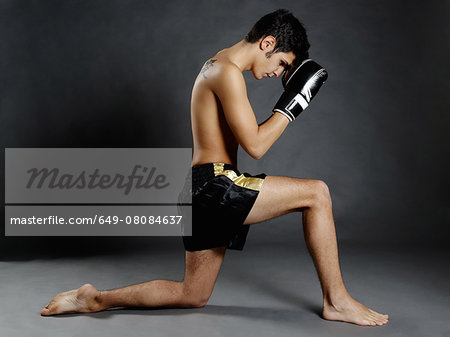 Studio portrait of young man with boxing gloves poised on one knee