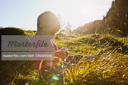 Baby girl sitting in field touching blades of grass
