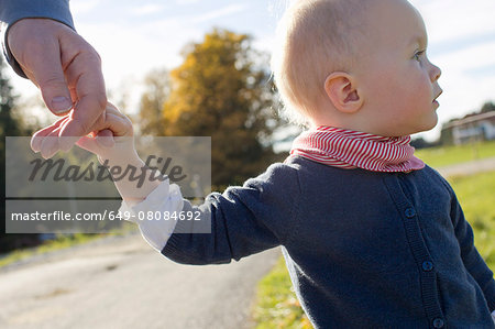 Baby girl toddling on rural road holding fathers hand