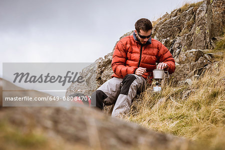 Young male hiker igniting camping stove, The Lake District, Cumbria, UK