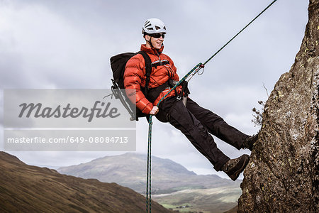 Young male climber abseiling down rock, The Lake District, Cumbria, UK