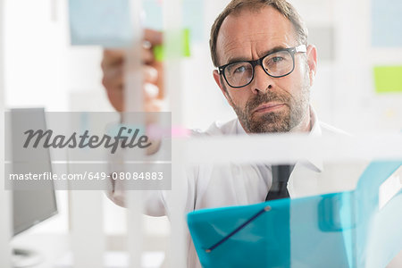 Businessman sticking adhesive notes to glass wall in office