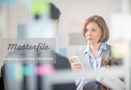 Mature businesswoman meeting with smartphone and blueprints in office