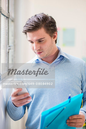 Young businessman reading texts on smartphone in office