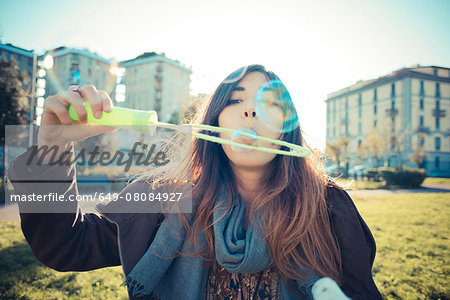 Portrait of mid adult woman blowing bubbles in park