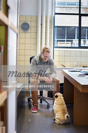 Young man looking down at cute dog from office desk