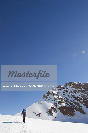 Rear view of man hiking across snow covered landscape, Jungfrauchjoch, Grindelwald, Switzerland