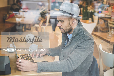 Businessman sitting in front of cafe window using laptop