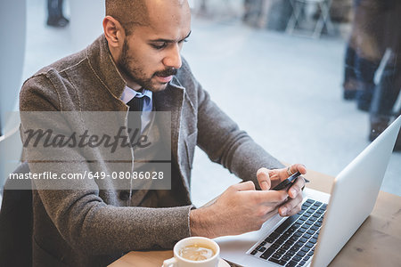 Businessman sitting in cafe texting on smartphone