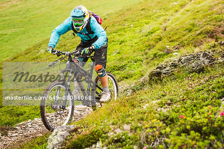 Young female mountain biker cycling on hillside track