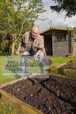 Senior man, digging soil in garden