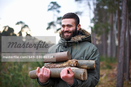 Young man collecting logs for campfire in forest