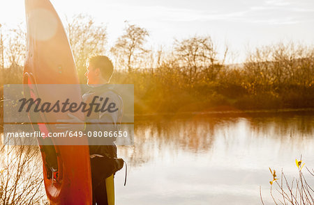 Young man holding kayak by lake