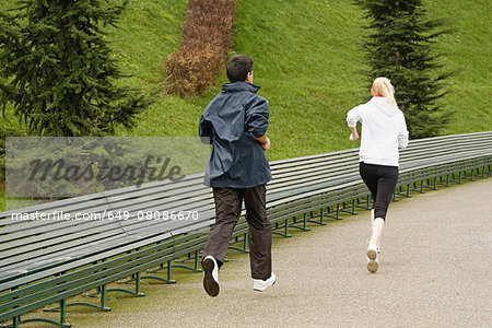 Man and woman running along pathway, rear view