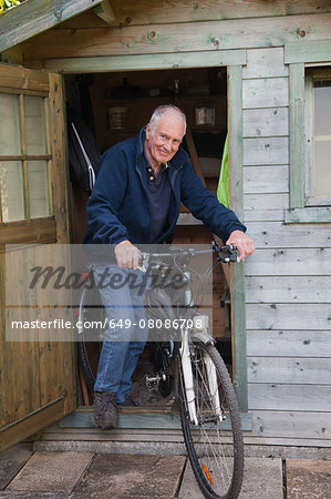 Senior man on bike by shed