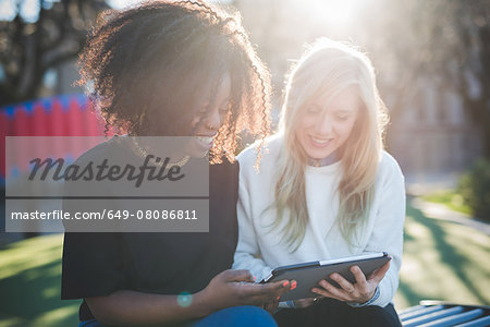 Two young female friends on park bench looking at digital tablet, Como, Italy