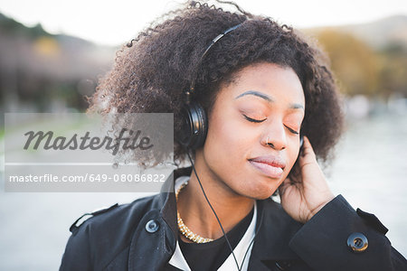Close up of young woman listening to headphones with eyes closed at Lake Como, Italy