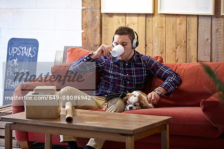 Mid adult man drinking coffee and petting dog in picture framers showroom