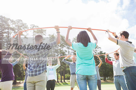 Team forming connected circle with plastic hoop in sunny field