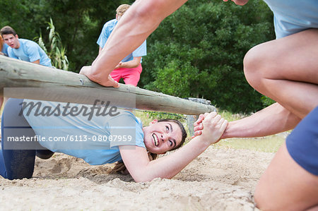 Teammate helping woman under log on boot camp obstacle course