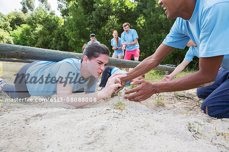 Teammate helping determined woman crawling on boot camp obstacle course