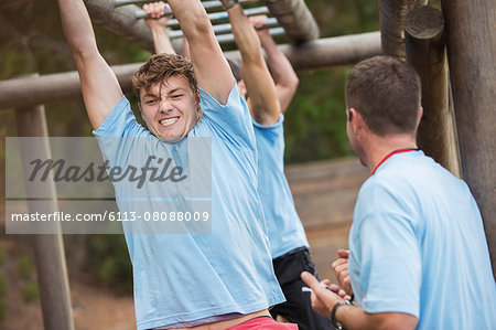 Determined man crossing monkey bars on boot camp obstacle course