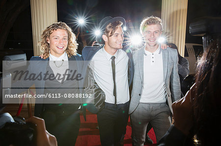Portrait of smiling celebrities being photographed by paparazzi at red carpet event