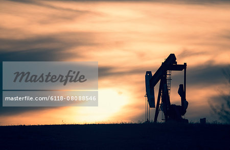 A pumpjack at an oil drilling site at sunset. A pumpjack at an oil drilling site at sunset.