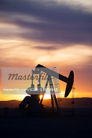 A pumpjack at an oil drilling site at sunset.