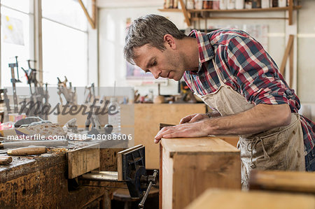 An antique furniture restorer in his workshop using a hand tool to smooth a wooden object.