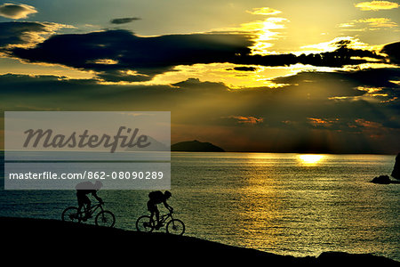 Mountain bikers on cliffs overlooking Red Beach in Matala, Crete, Greece, Europe, MR