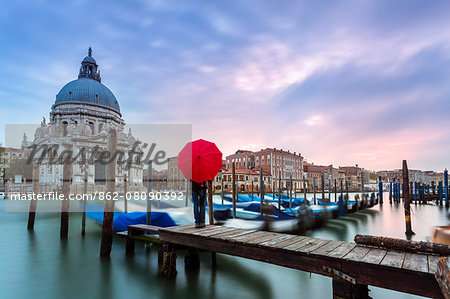 Italy, Veneto, Venice. Santa Maria della Salute church on the Grand Canal, at sunset, woman standing with red umbrella (MR)