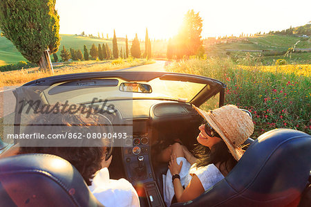 Italy, Tuscany, Siena district, Orcia Valley, Montichiello. A young couple driving in a winding road and cypresses.(MR)