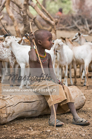 Kenya, Marsabit County, Lasien. A young Samburu girl sits on a log at Lasien wells after her family' s livestock has been watered. Her sandals are made from old rubber tyres.