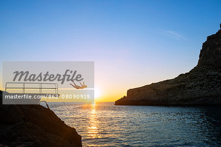 Mediterranean Europe, Malta, Gozo Island, resort town of Xlendi, swimmer diving into Xlendi bay at sunset