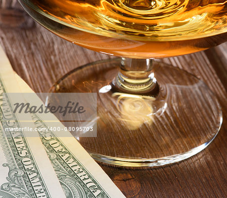 Close up luxury still life with glass of cognac and dollar bills on a wood background. Top view. High resolution