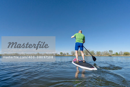 senior male on SUP (stand up paddleboard) on a lake under Colorado blue sky