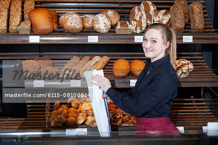 Female shop assistant in bakery packing bread into bag