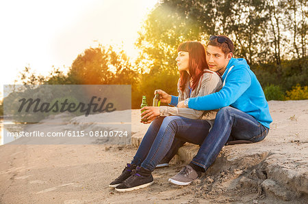 Young couple embracing and drinking beer on riverbank, Osijek, Croatia