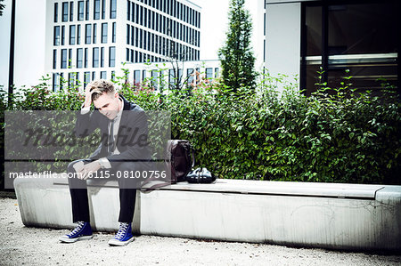 Young businessman sitting with hand in hair, Munich, Bavaria, Germany