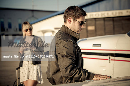 Pilot checking wing of propeller airplane, woman is watching