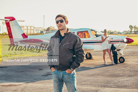 Young man on airfield, woman by airplane in background