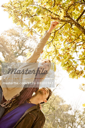 Young couple picking autumn leaf from tree