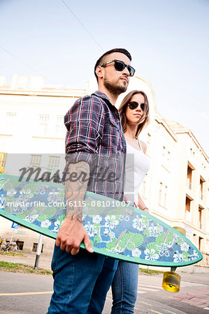 Young couple with skateboard walking in town