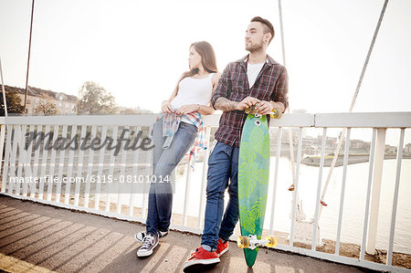 Young couple with skateboard waiting on bridge