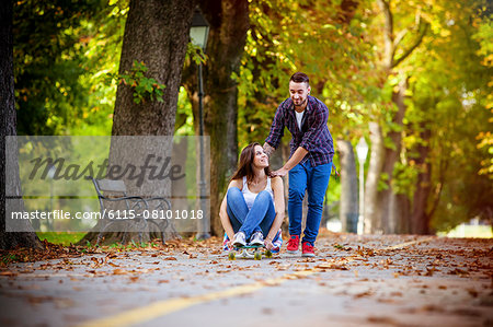 Young couple skateboarding through park