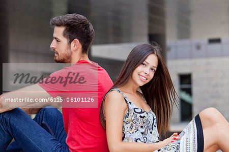 Happy young couple sits back to back on campus