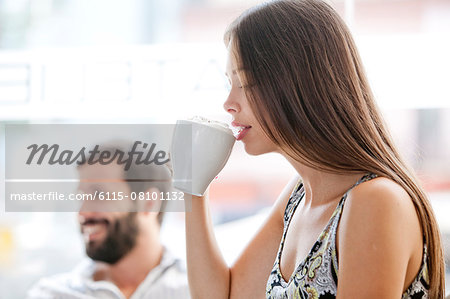 Young woman having a cappuccino, man in background