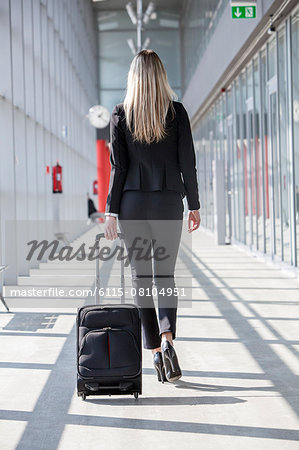 Businesswoman pulling luggage in modern lobby, rear view